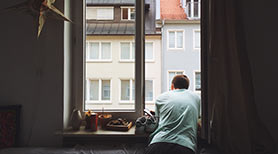 Mand i lejlighed kigger ud af åbent vindue i lejlighed og ned på gaden
